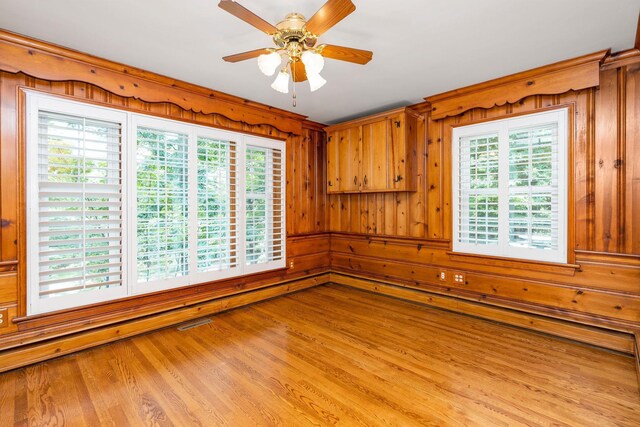 spare room featuring light hardwood / wood-style flooring, a wealth of natural light, ceiling fan, and wood walls