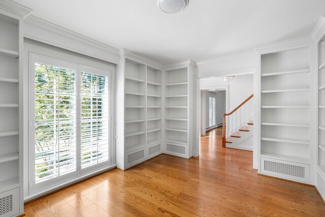 unfurnished room featuring built in shelves, ornamental molding, and light hardwood / wood-style floors