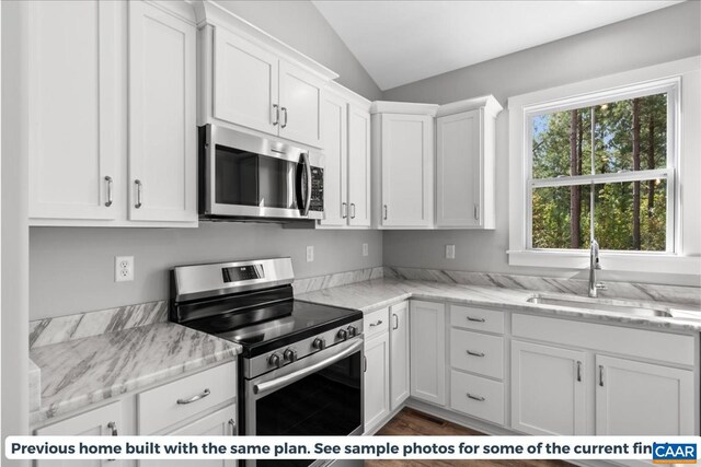 kitchen with sink, appliances with stainless steel finishes, white cabinetry, light stone counters, and vaulted ceiling