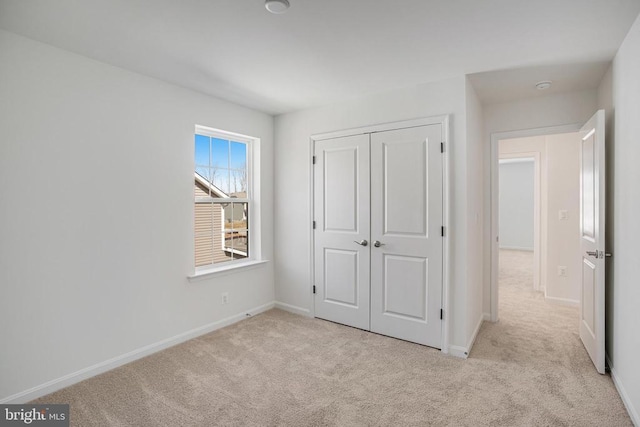 unfurnished bedroom featuring light carpet, a closet, and baseboards