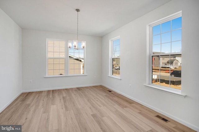 unfurnished dining area featuring an inviting chandelier, plenty of natural light, baseboards, and light wood finished floors