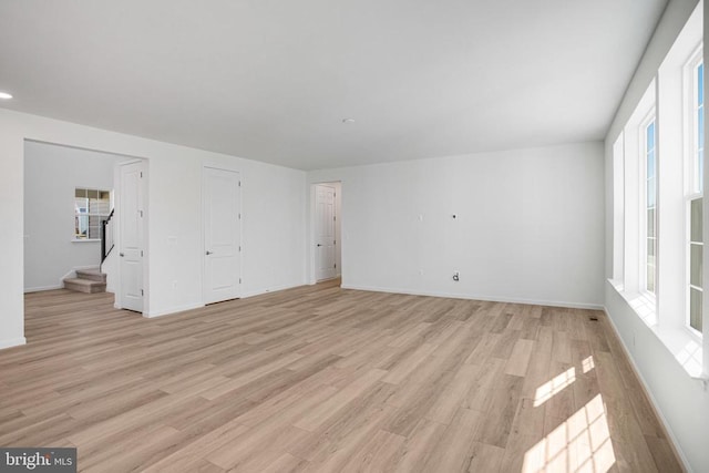 unfurnished living room with light wood finished floors, baseboards, and stairway