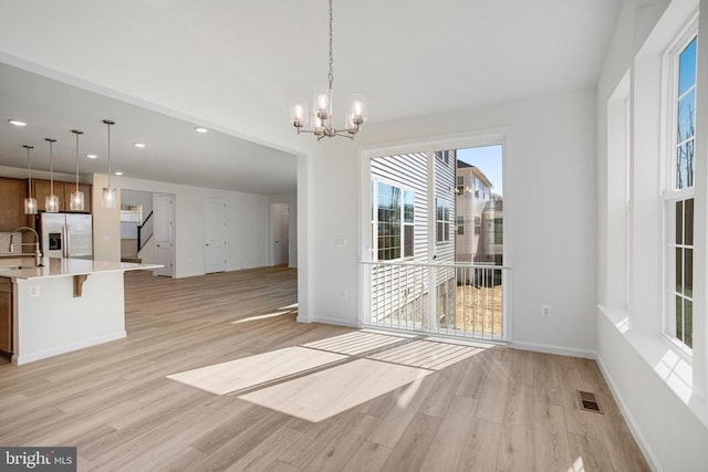 unfurnished dining area with light wood-type flooring, visible vents, a chandelier, and a sink