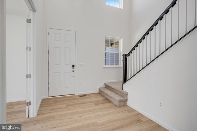 foyer featuring light wood-style flooring, a high ceiling, visible vents, baseboards, and stairway