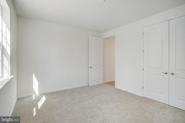 unfurnished bedroom featuring baseboards, a closet, and light colored carpet