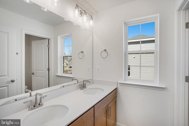 bathroom with toilet, double vanity, and a sink