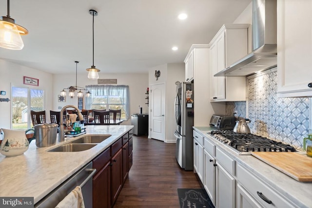 kitchen with sink, decorative light fixtures, appliances with stainless steel finishes, wall chimney range hood, and white cabinets