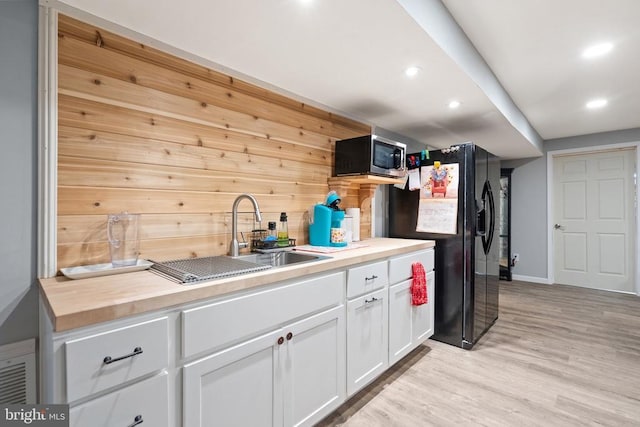 kitchen with sink, butcher block countertops, white cabinetry, black refrigerator with ice dispenser, and light hardwood / wood-style flooring