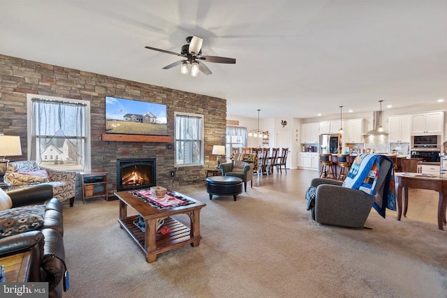 carpeted living room featuring ceiling fan and a stone fireplace