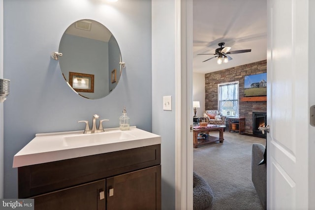 bathroom with vanity, a stone fireplace, and ceiling fan