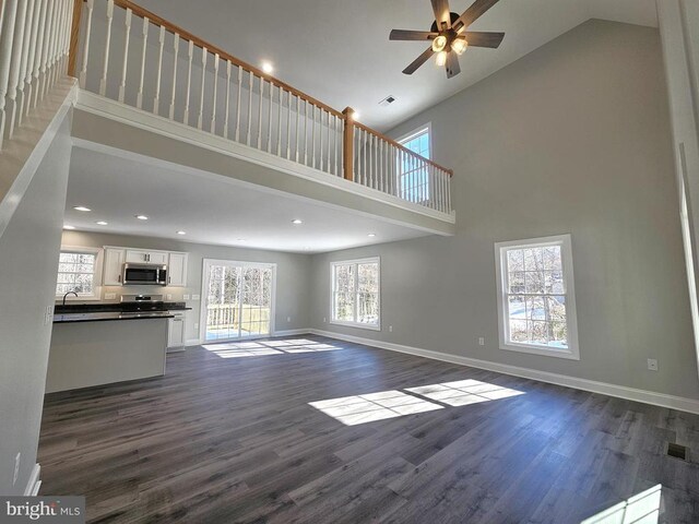 unfurnished living room featuring a towering ceiling, baseboards, visible vents, and dark wood-type flooring