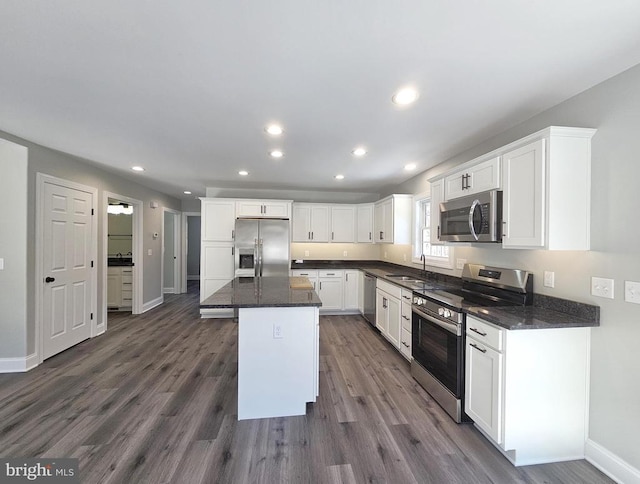 kitchen featuring a sink, white cabinetry, appliances with stainless steel finishes, a center island, and dark stone counters