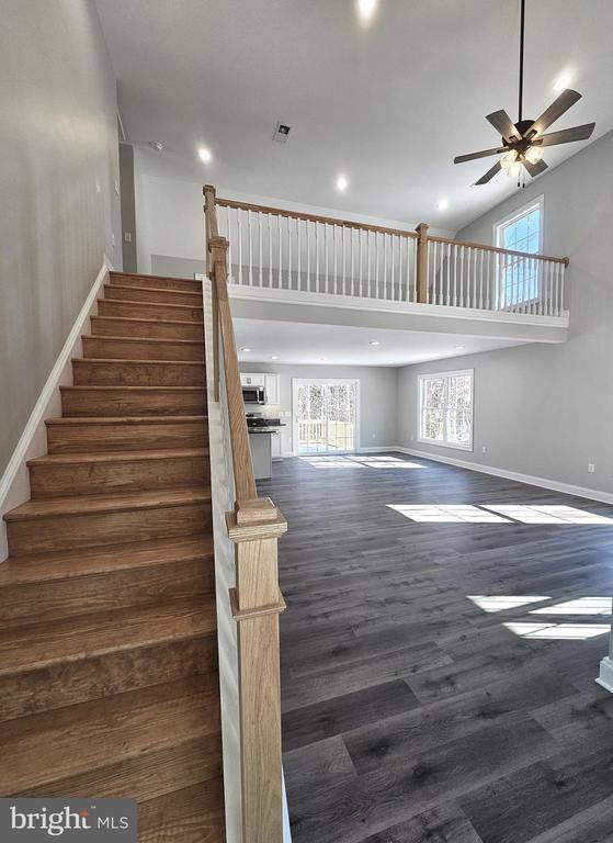 stairway with baseboards, a ceiling fan, wood finished floors, a high ceiling, and recessed lighting