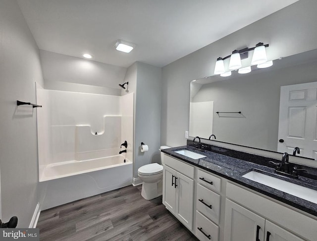 bathroom with toilet, shower / washtub combination, a sink, and wood finished floors