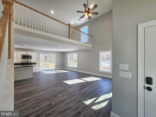 unfurnished living room with dark hardwood / wood-style flooring, ceiling fan, and a high ceiling