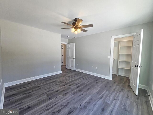 unfurnished bedroom featuring a closet, dark wood finished floors, a spacious closet, and baseboards