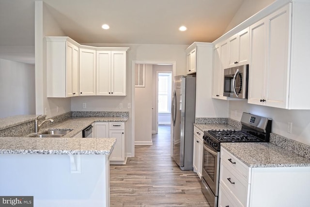 kitchen with stainless steel appliances, white cabinetry, a sink, light stone countertops, and a peninsula