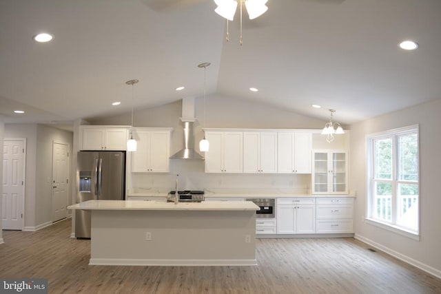 kitchen featuring white cabinets, appliances with stainless steel finishes, light wood-type flooring, wall chimney exhaust hood, and an island with sink