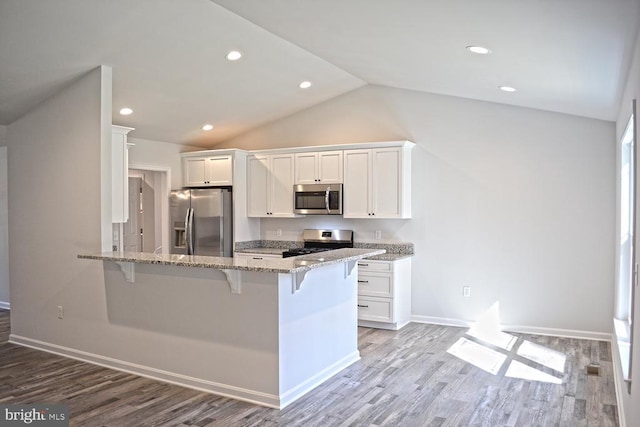 kitchen with a peninsula, white cabinetry, a kitchen breakfast bar, appliances with stainless steel finishes, and light stone countertops