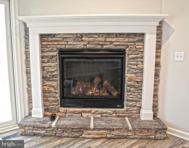 interior details featuring a stone fireplace, wood finished floors, visible vents, and baseboards