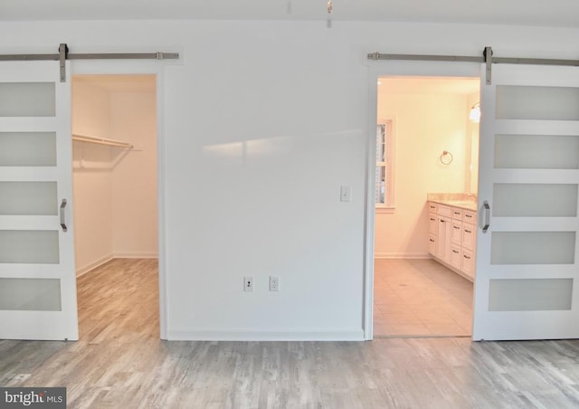 unfurnished bedroom with a barn door, a spacious closet, light wood-style flooring, and a closet