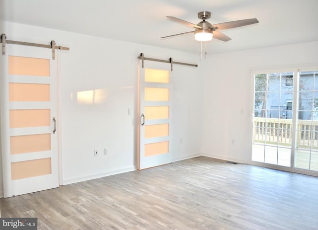 empty room with wood finished floors, visible vents, ceiling fan, and a barn door