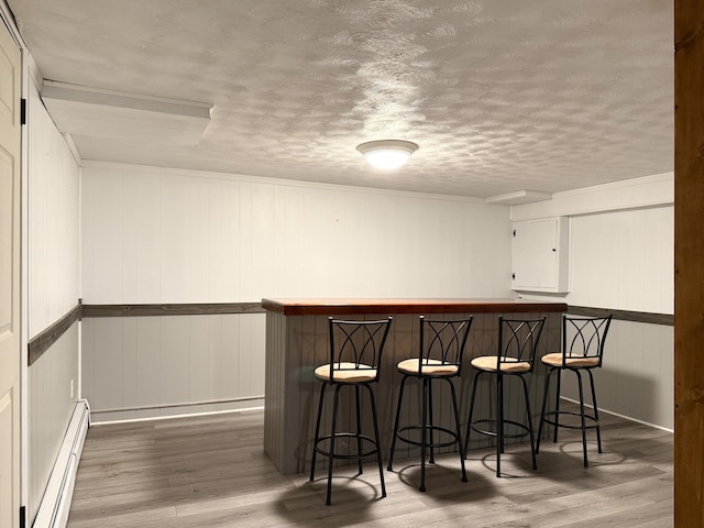 bar with wood finished floors, a textured ceiling, a bar, and a baseboard radiator