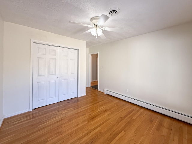 unfurnished bedroom featuring visible vents, a textured ceiling, a closet, light wood-style floors, and a baseboard radiator