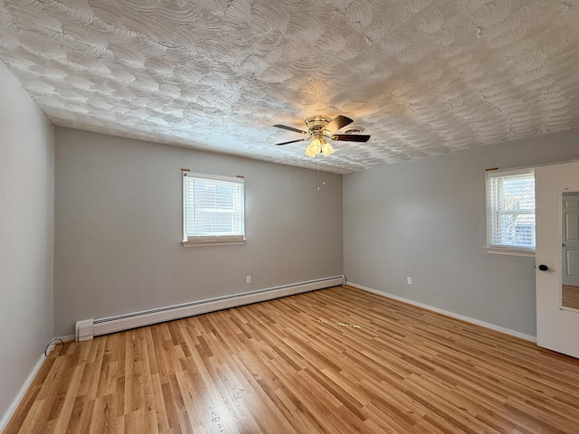 spare room with a baseboard heating unit, baseboards, light wood-style floors, and a textured ceiling