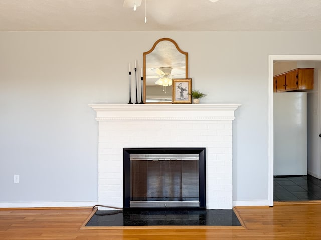 room details featuring a brick fireplace, freestanding refrigerator, a ceiling fan, and wood finished floors