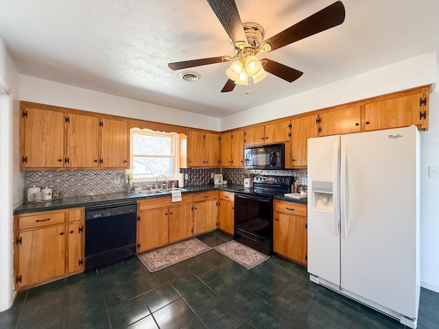 kitchen with visible vents, black appliances, a sink, dark countertops, and brown cabinetry