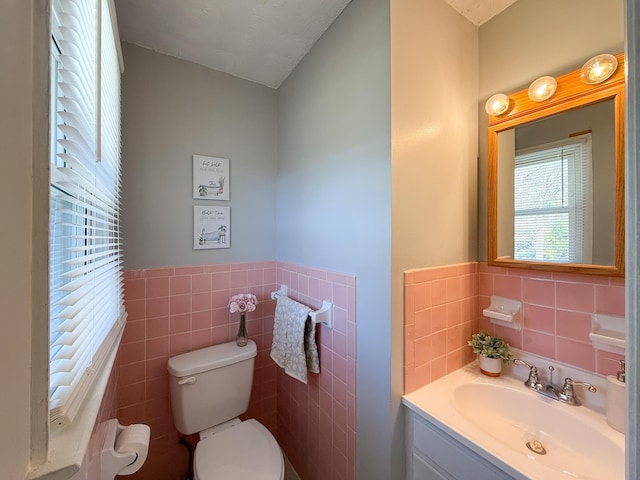 half bath with wainscoting, vanity, toilet, and tile walls