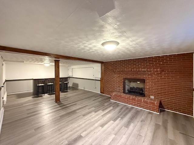 finished below grade area featuring a textured ceiling, wood finished floors, a bar, brick wall, and a fireplace