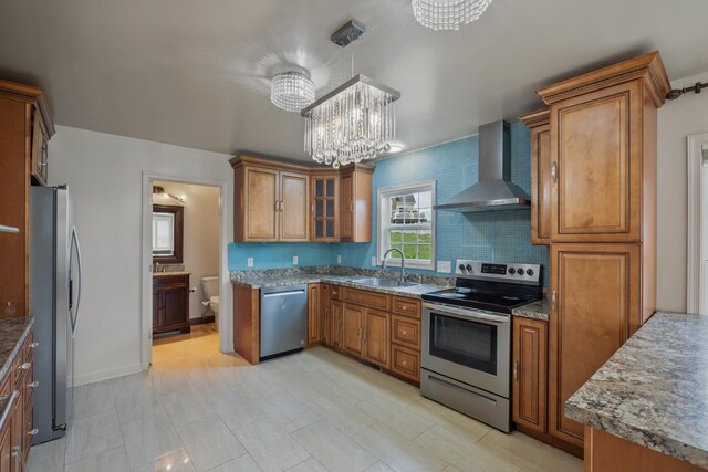 kitchen with pendant lighting, sink, a chandelier, stainless steel appliances, and wall chimney range hood