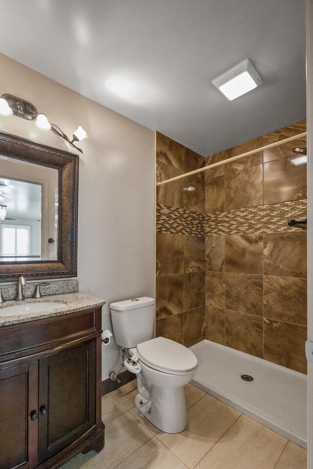 bathroom featuring tile patterned flooring, vanity, toilet, and tiled shower