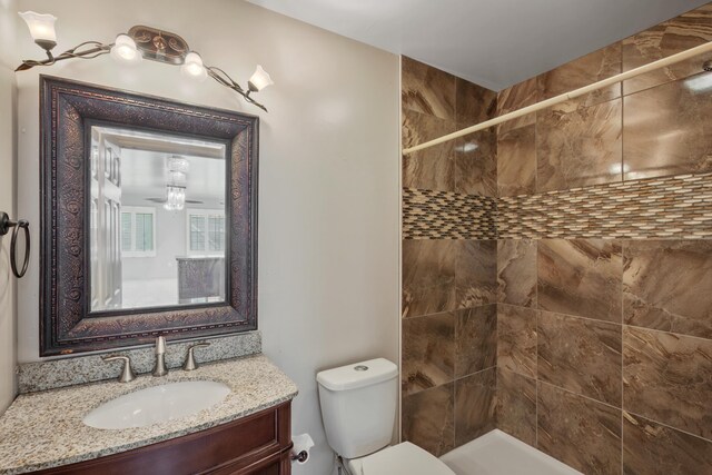 bathroom featuring a tile shower, vanity, and toilet