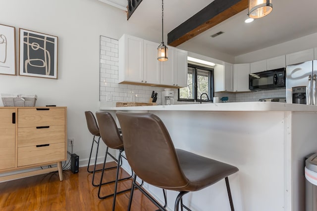 kitchen with black microwave, light countertops, a kitchen bar, and decorative backsplash