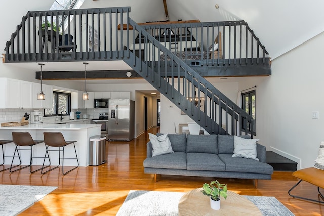 living area with high vaulted ceiling, beam ceiling, light wood-style flooring, and stairs