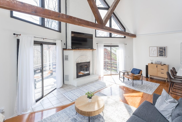 living area featuring high vaulted ceiling, a brick fireplace, visible vents, and wood finished floors