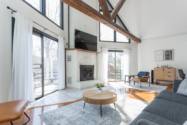 living room featuring visible vents, light wood-style floors, a fireplace, high vaulted ceiling, and beam ceiling