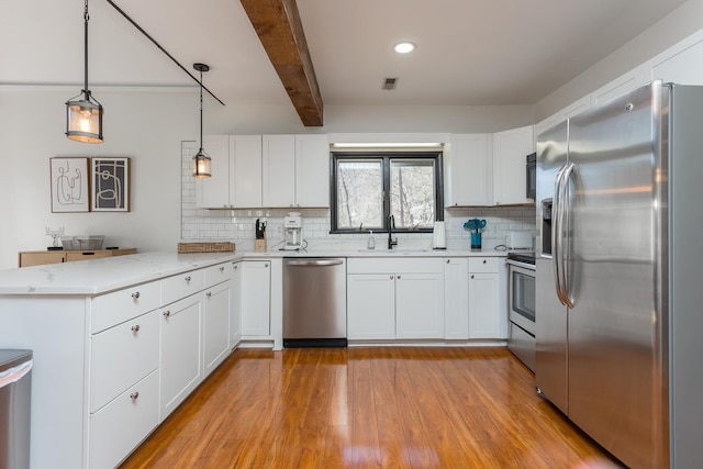 kitchen with appliances with stainless steel finishes, a peninsula, a sink, light wood-type flooring, and beam ceiling