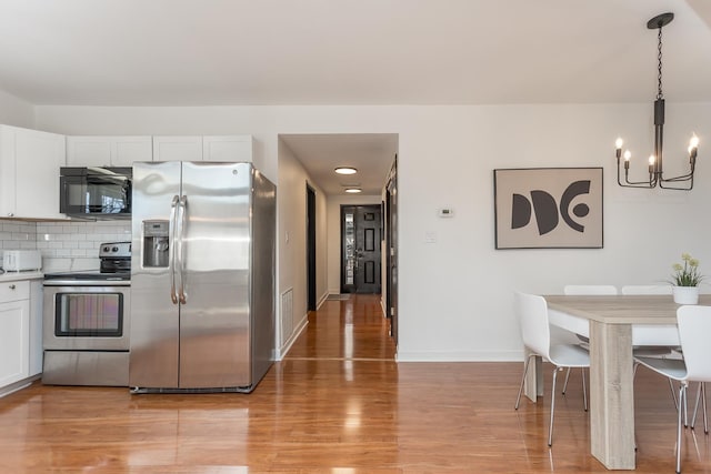 kitchen featuring light wood-style flooring, a notable chandelier, white cabinetry, appliances with stainless steel finishes, and backsplash