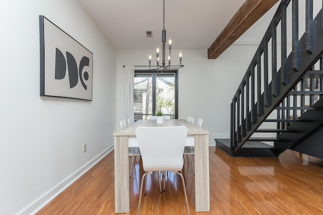 dining room featuring beam ceiling, stairway, wood finished floors, a chandelier, and baseboards