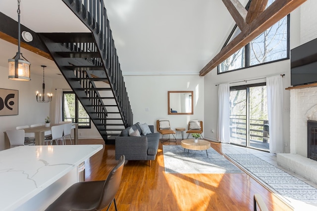 living room featuring high vaulted ceiling, a fireplace, wood finished floors, stairway, and an inviting chandelier