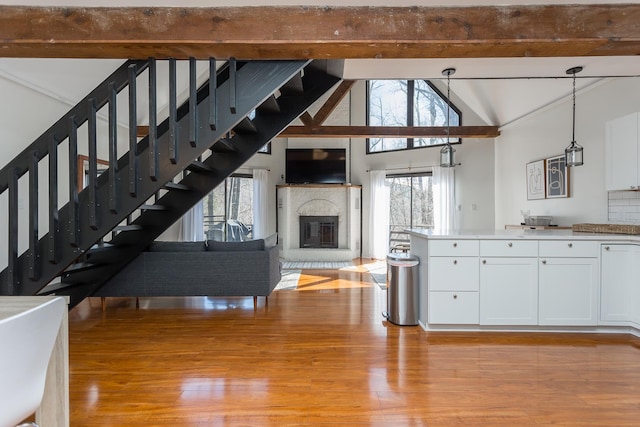 unfurnished living room featuring light wood-style floors, stairs, a brick fireplace, and beamed ceiling