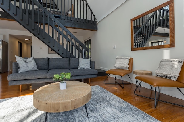 living area with stairway, wood finished floors, a towering ceiling, and baseboards