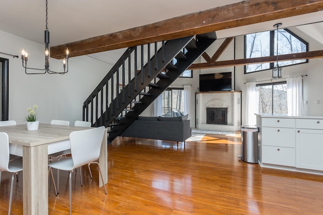 unfurnished dining area featuring vaulted ceiling with beams, light wood finished floors, stairway, a glass covered fireplace, and a chandelier