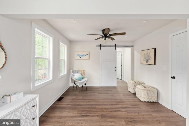sitting room with visible vents, a barn door, baseboards, and wood finished floors