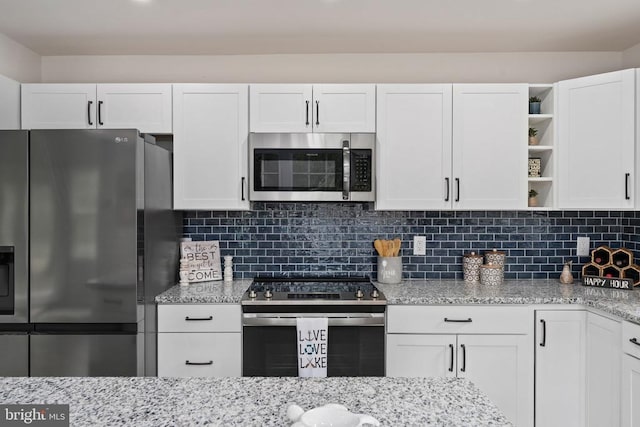 kitchen with light stone counters, white cabinets, open shelves, and stainless steel appliances
