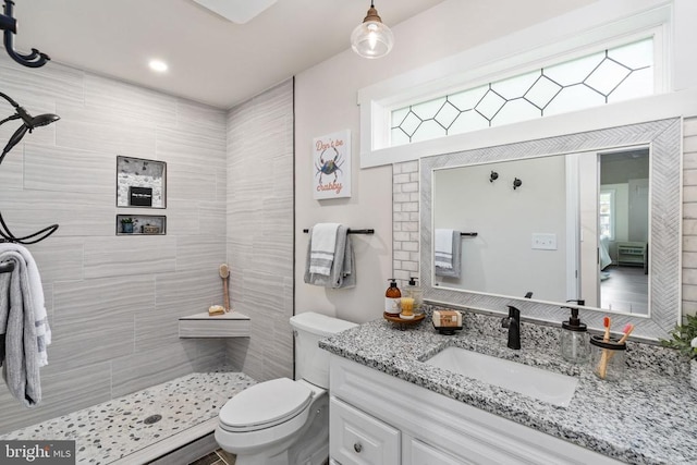 bathroom with toilet, a tile shower, and vanity